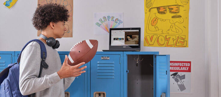 Student handles football while looking at laptop sitting on top of an open locker