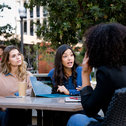 Group of college students in conversation around outdoor table on campus